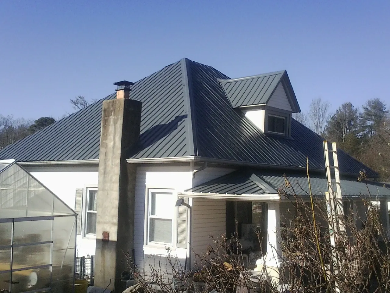 Dark blue standing seam metal roof on a white farmhouse with dormer — Slate & Tile Roof Repair by Roofing Brothers in Bolivar