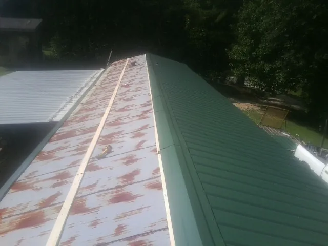 Old rusted panels beside newly installed green metal roofing — Wind Damage Roof Repair by Roofing Brothers in Bolivar