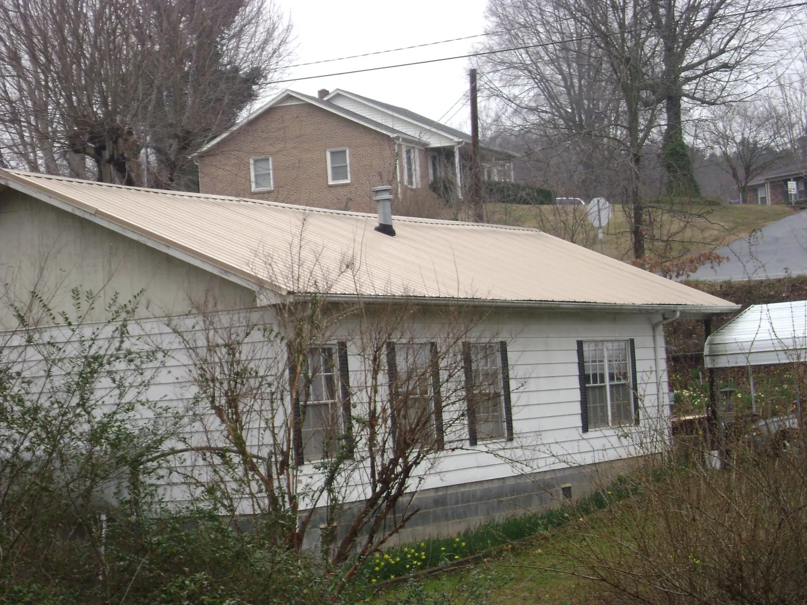 Tan metal roof on a white sided house set into a hillside — Commercial Roofing by Roofing Brothers in Bolivar